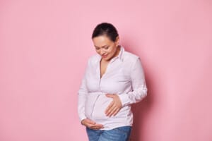 Uśmiechnięta kobieta w ciąży, delikatnie trzymająca się za brzuch, symbolizująca radość z ciąży po 40 roku życia