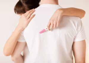 Kobieta przytula meżczyznę, trzymając test ciążowy