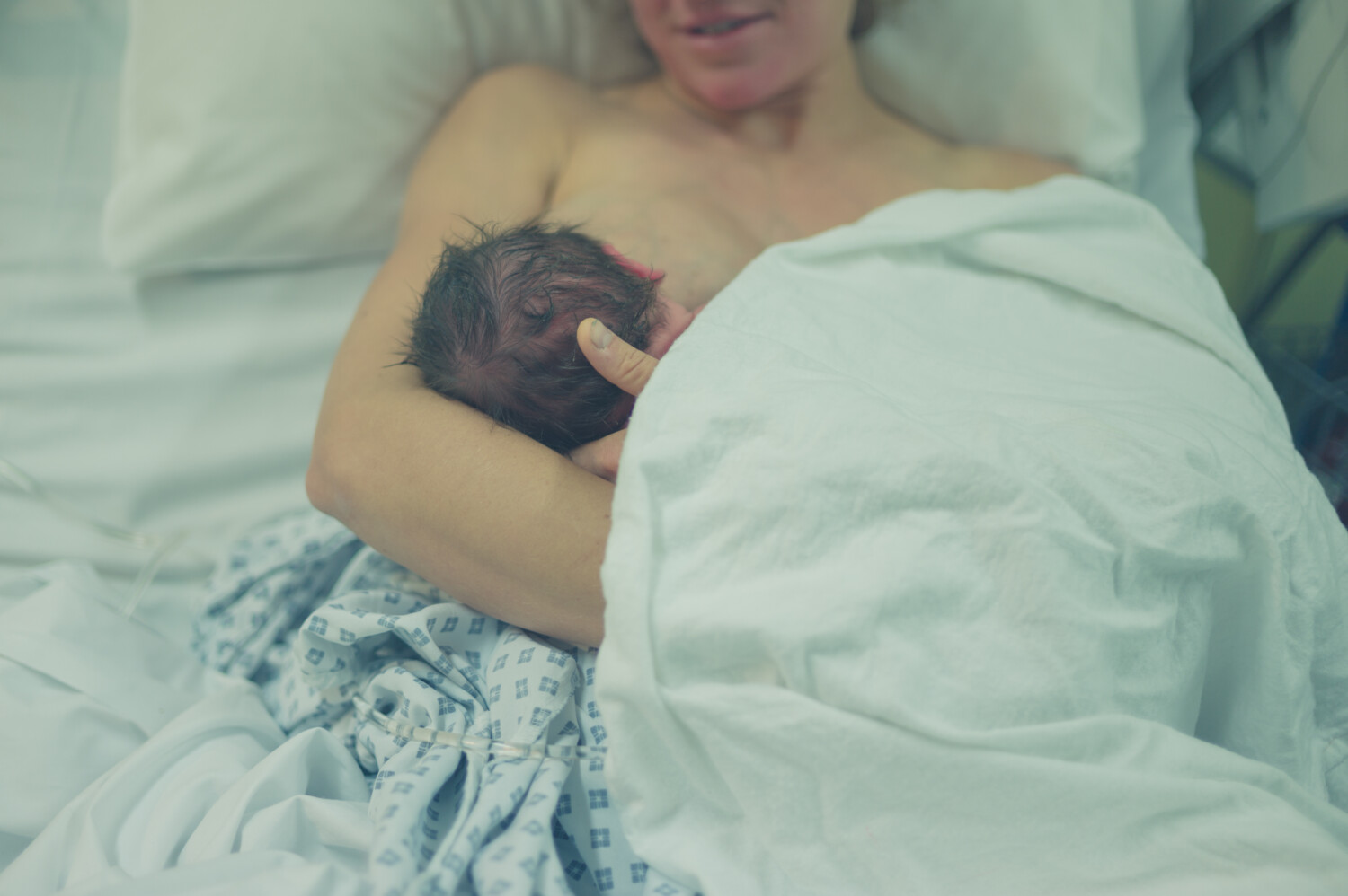 Kobieta leży w łożku i karmi noworodka piersią