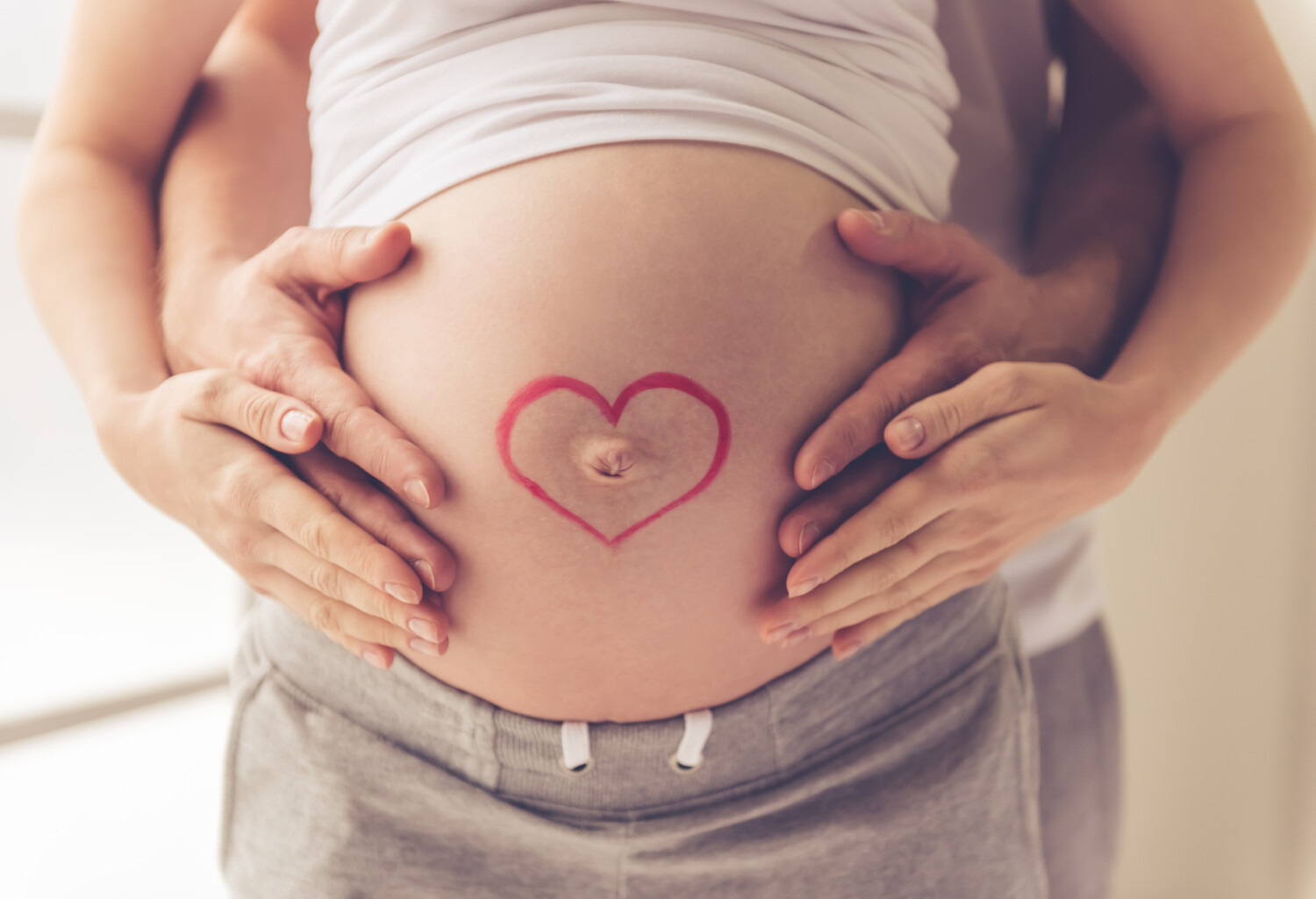 Kobieta w ciąży, z mężczyzną obejmującym rękami jej brzuch